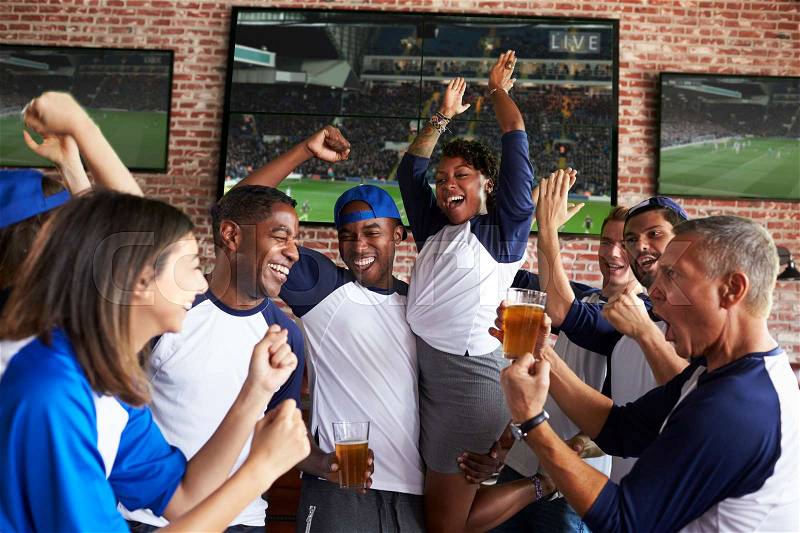 Friends Watching Game In Sports Bar On Screens Celebrating, stock photo
