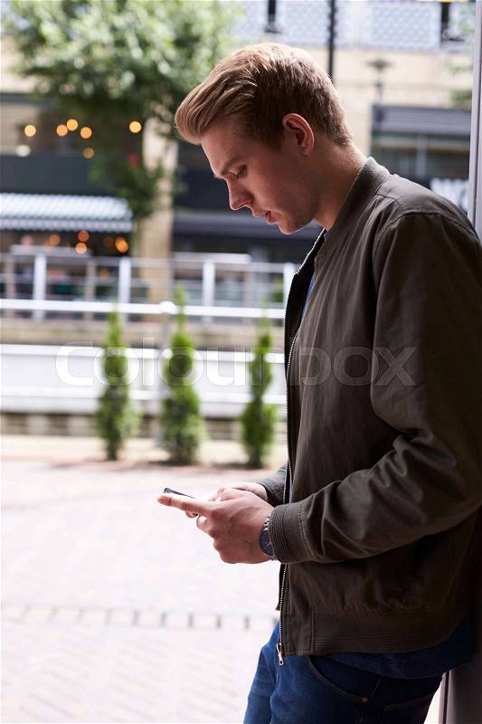 Man Sending Text Message On Mobile Phone In Urban Setting, stock photo
