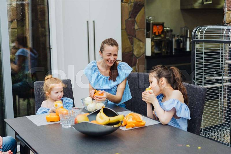 Mom and daughter in the kitchen eating oranges, stock photo