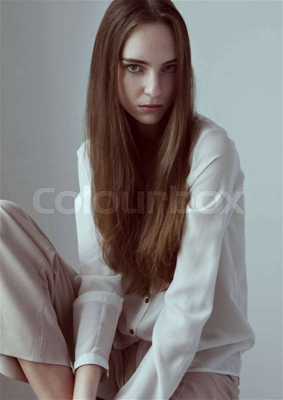 Model test with young beautiful fashion model with long hair wearing white shirt on grey background, stock photo