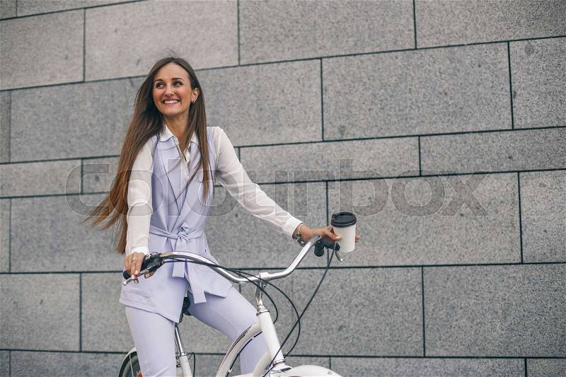 Beautiful young woman on bicycle with coffee. Businesswoman smiling and cycling to work, stock photo