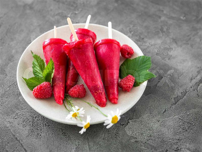 Plate full of homemade ice cream shaped into cones, made with raspberries, served on sticks, stock photo