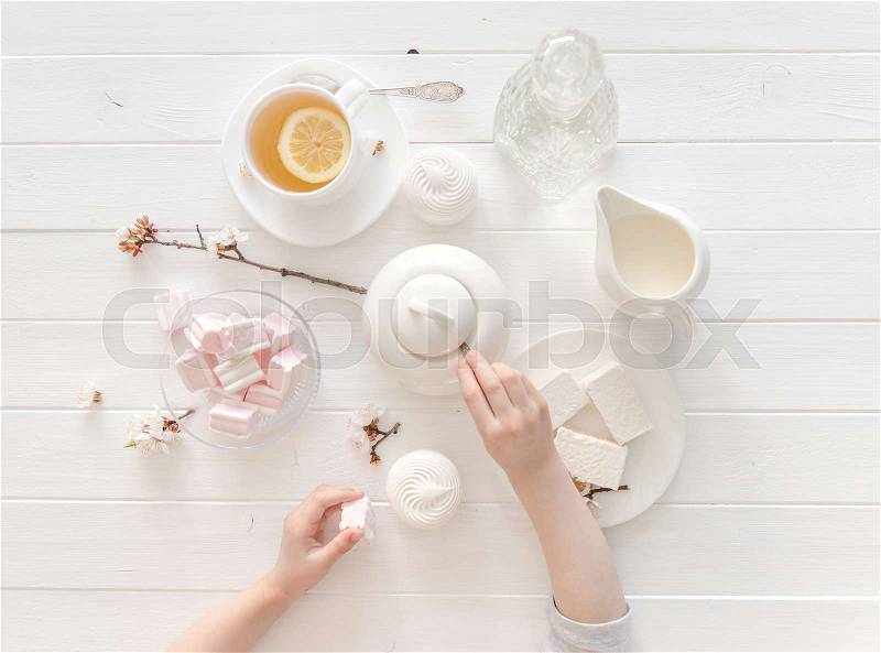 Tiny hands holding sweets for tea ceremony in pastel pink and white colors, porcelain, topview, stock photo