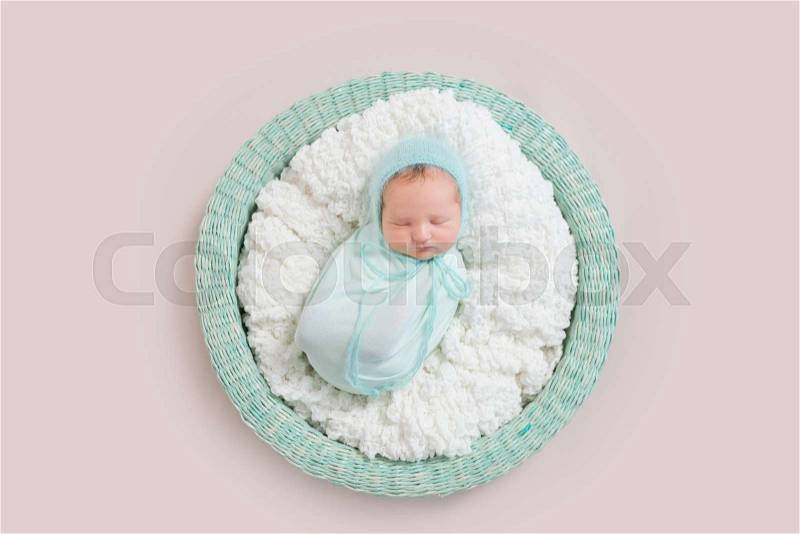 Adorable baby wrapped in blue blanket sleeping on white and blue bedding, in basket, topview, stock photo