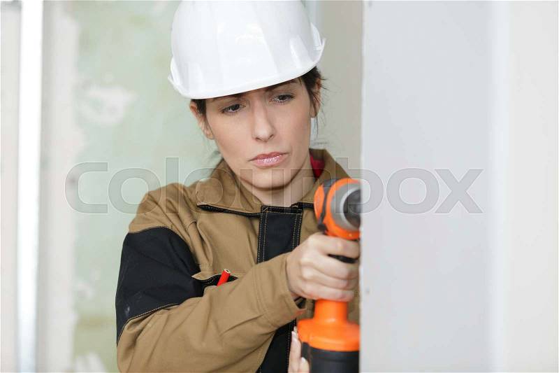 Woman drilling wall in new house, stock photo