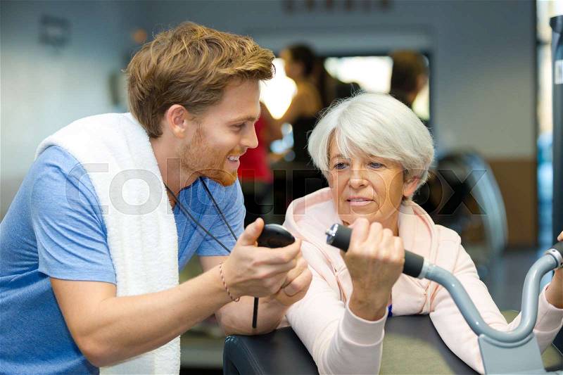 Trainer encouraging senior woman exercising, stock photo