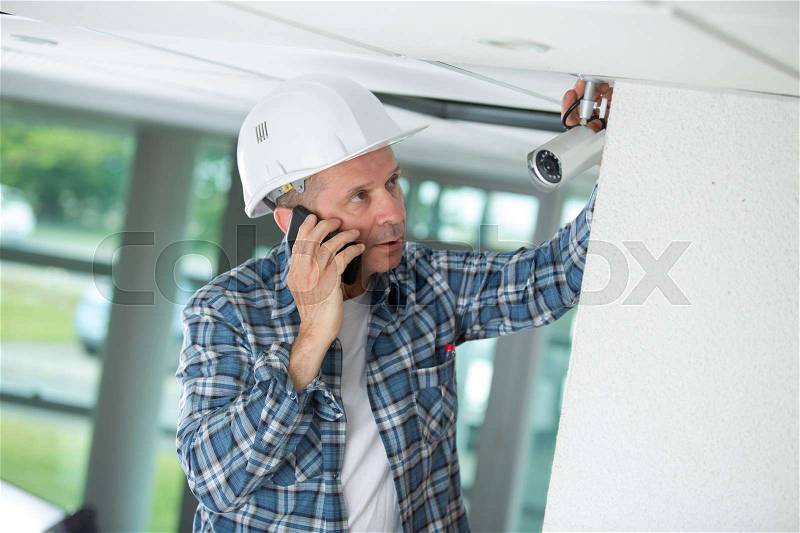 Worried male technician installing camera on wall, stock photo