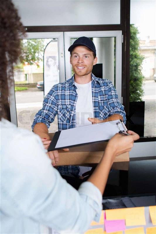 Smiling delivery man and young woman signing clipboard, stock photo