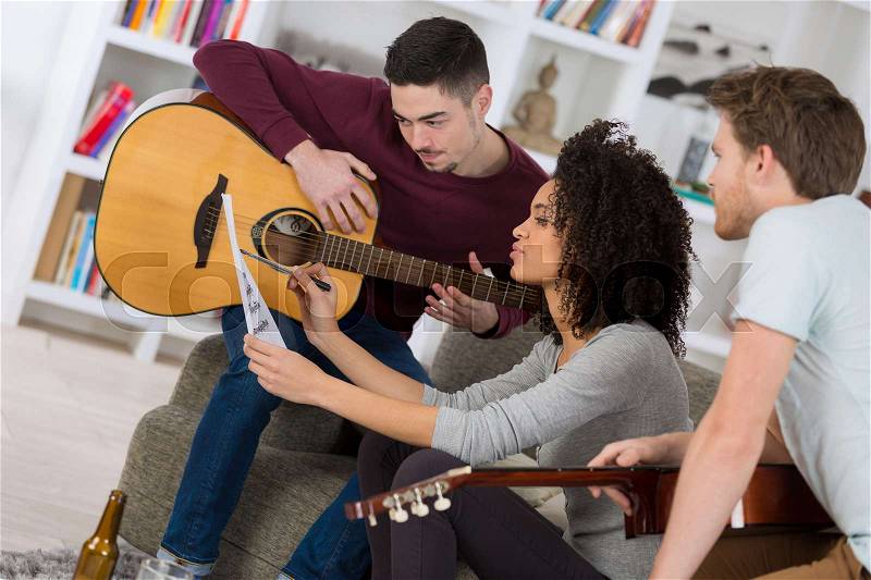 Happy friends playing guitar and listening to music at home, stock photo