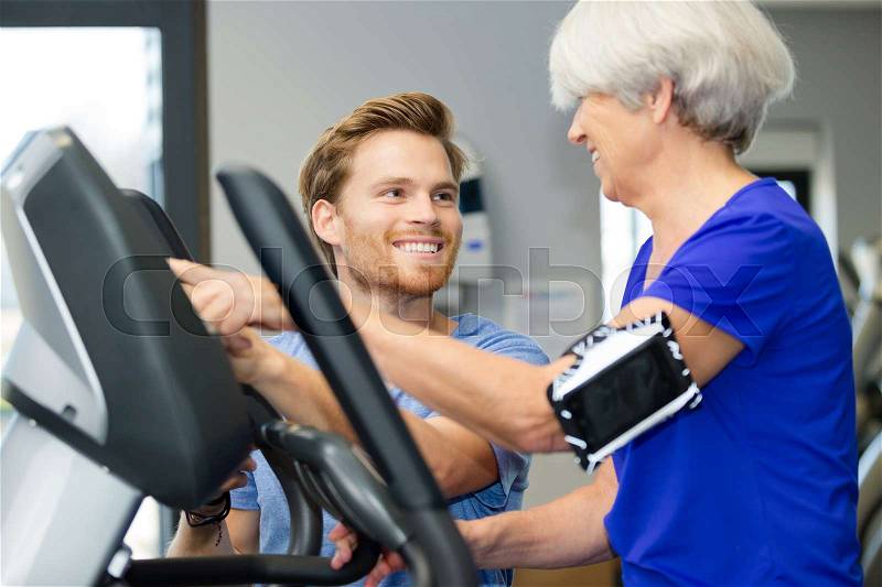 Instructor aiding senior woman in gym, stock photo