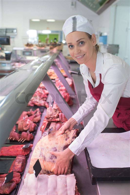 Female butcher in meat store counter, stock photo