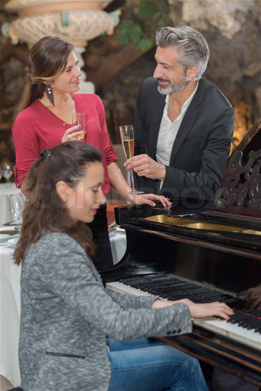 Couple enjoying glass of champagne while woman plays piano, stock photo