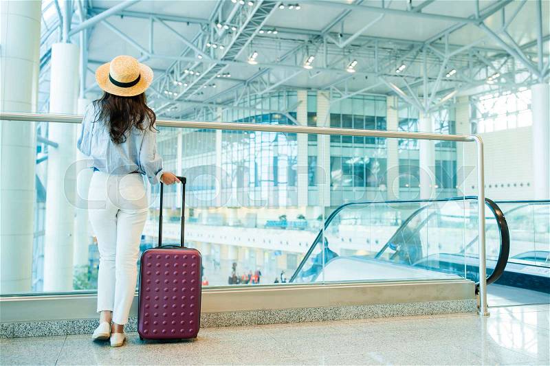 Young woman in hat with baggage in international airport walking with her luggage. Airline passenger in an airport lounge waiting for flight aircraft, stock photo