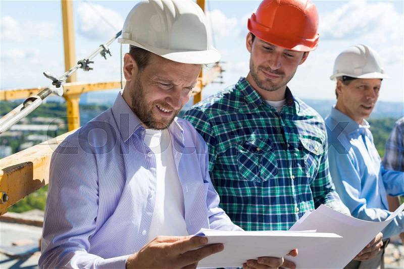 Architect And Builders Looking At Buiding Plan Blueprint Wearing Hardhat While Meeting On Construction Site, Team Of Engineers Communication, stock photo