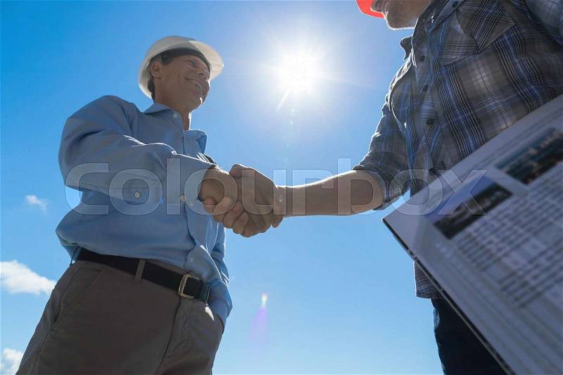 Builders Handshake, Architect And Contractor Agreement During Meeting Discussing Blueprint Buiding Plan On Construction Site, stock photo