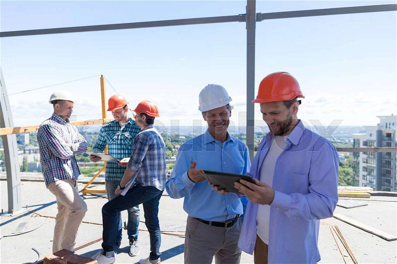 Builders On Site Holding Tablet Computer Discuss Construction Project Over Team Of Apprentices Talking Teamwork Concept, stock photo