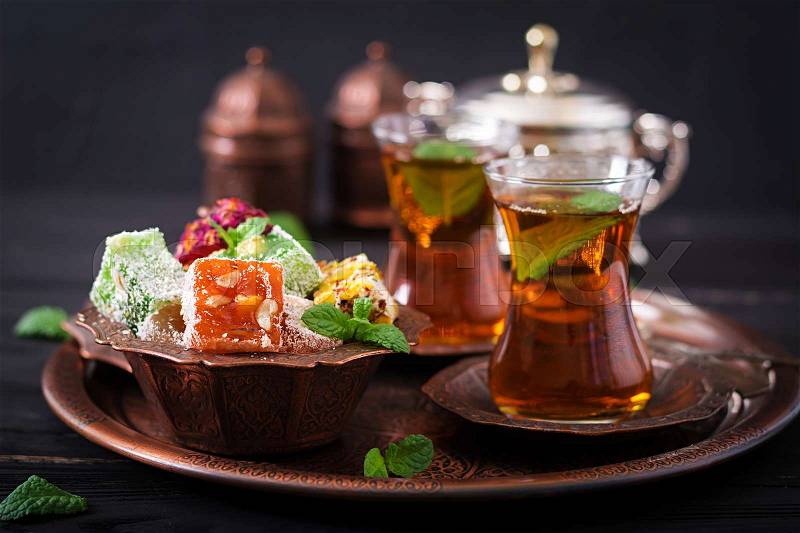 Bowl with various pieces of turkish delight lokum and black tea with mint on a dark background, stock photo
