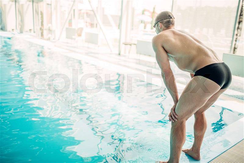 Athletic male swimmer at the curb, back view. indoor swimming pool. Aqua sports exercise, stock photo