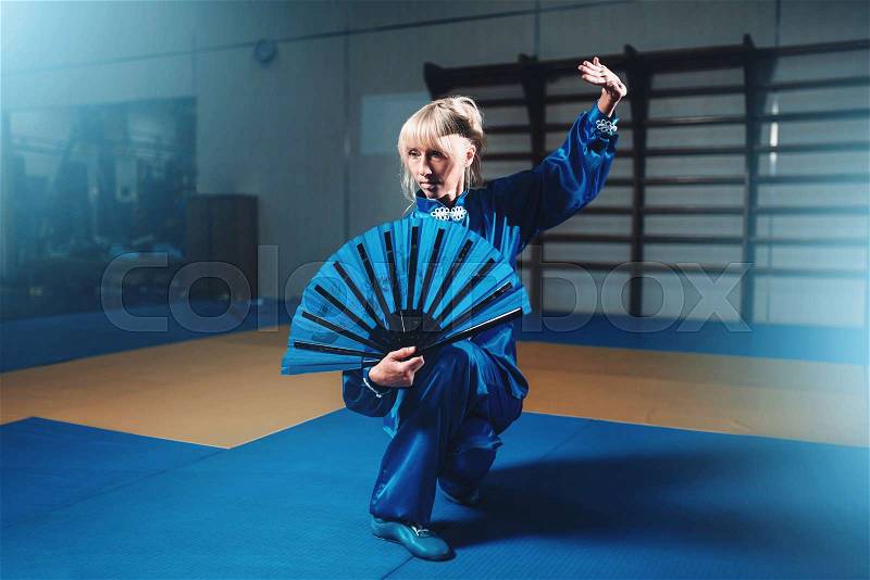 Female wushu master with fan, martial arts. Woman in blue cloth on fight training, stock photo