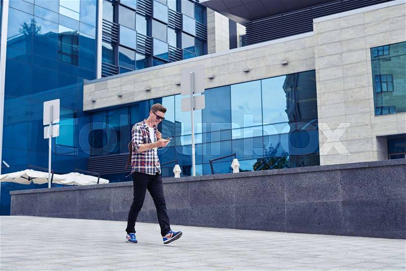 Wide shot of stylish young man listens to music and enjoys city panorama. Walking in front of business mall , stock photo