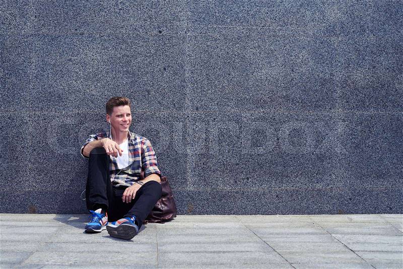 Mid shot of good-looking man leaning on wall while listening to the music. Handsome man resting outdoors , stock photo
