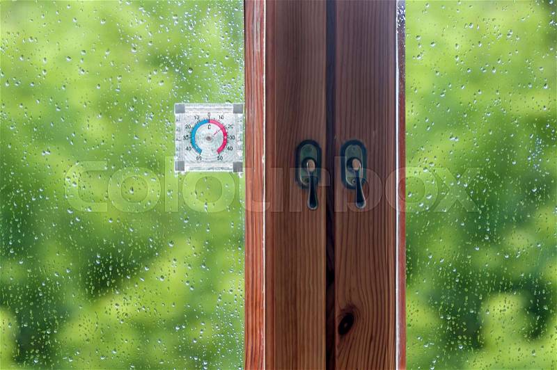 Drops of rain on a wooden window and a thermometer, green background, stock photo