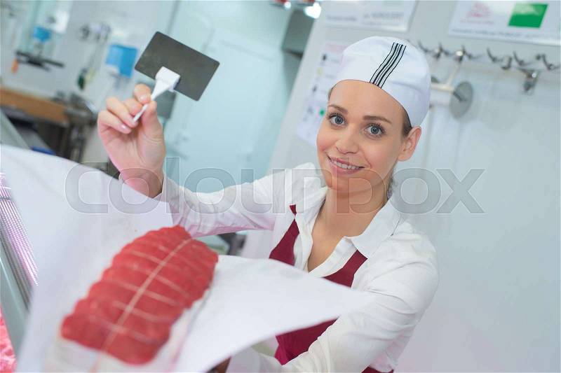 Female butcher holding joint of beef and blank label, stock photo