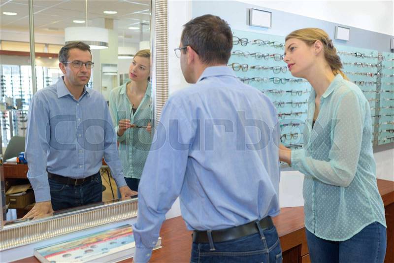 Man trying on spectacles and looking in mirror, stock photo