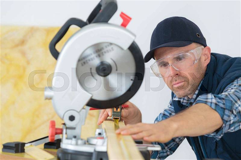 Workman using tape measure under circular saw, stock photo
