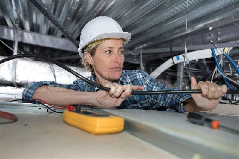 Female electrician working in confined space, stock photo