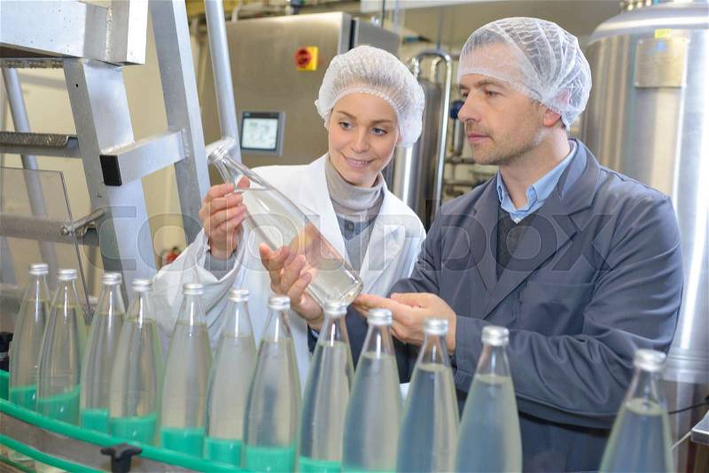 Man and woman examining bottle in factory, stock photo