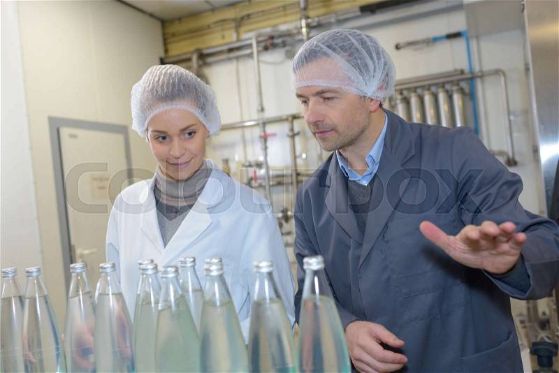 People in factory looking at glass bottles, stock photo