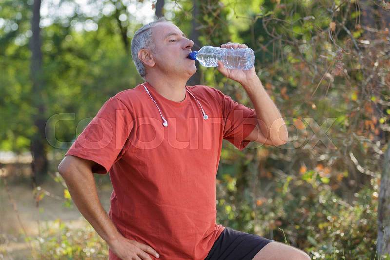 Middle aged man drinking water from bottle, stock photo