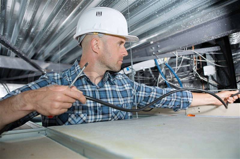 Electrician installing cable in roof space, stock photo