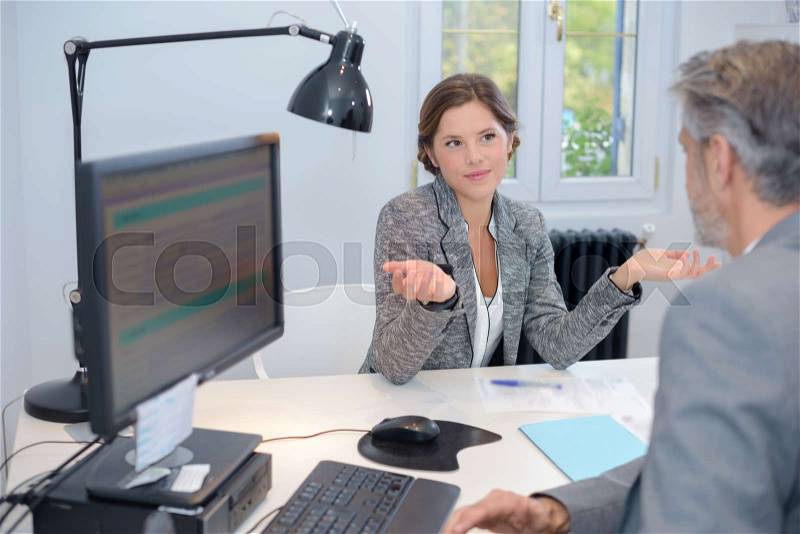 Businesswoman making questioning gesture to male colleague, stock photo