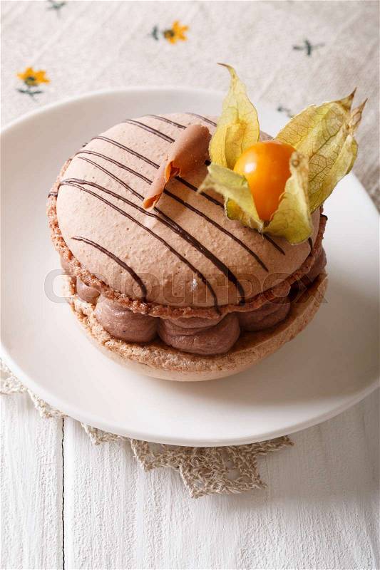 Beige delicious macaroon with chocolate cream decorated cape gooseberry close-up on a plate. vertical , stock photo