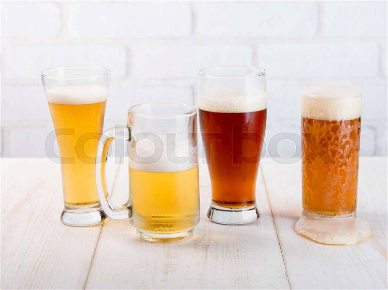 Beer glasses with various beer on wood table against white brick wall, stock photo