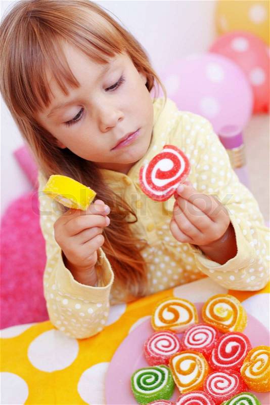 Cute child eating candies at home, stock photo