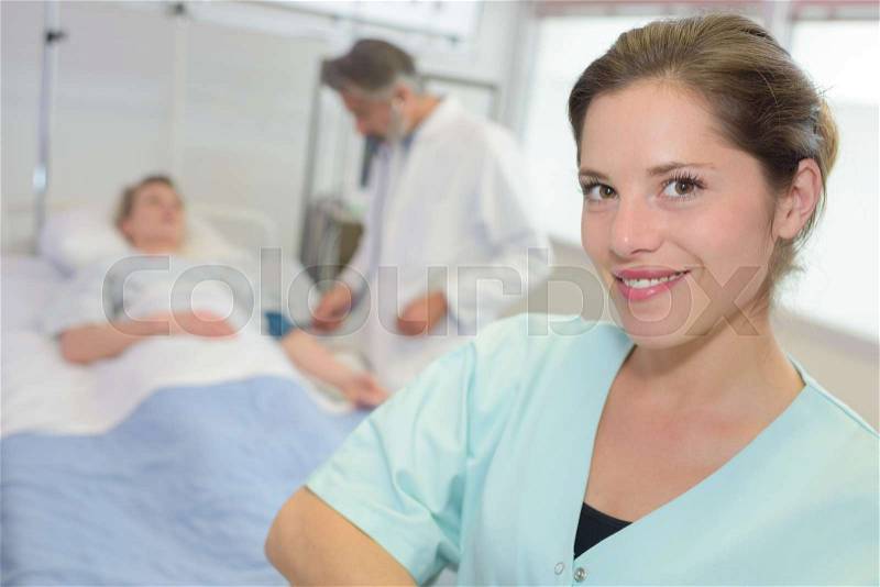 Portrait of nurse, patient in hospital bed in the background, stock photo