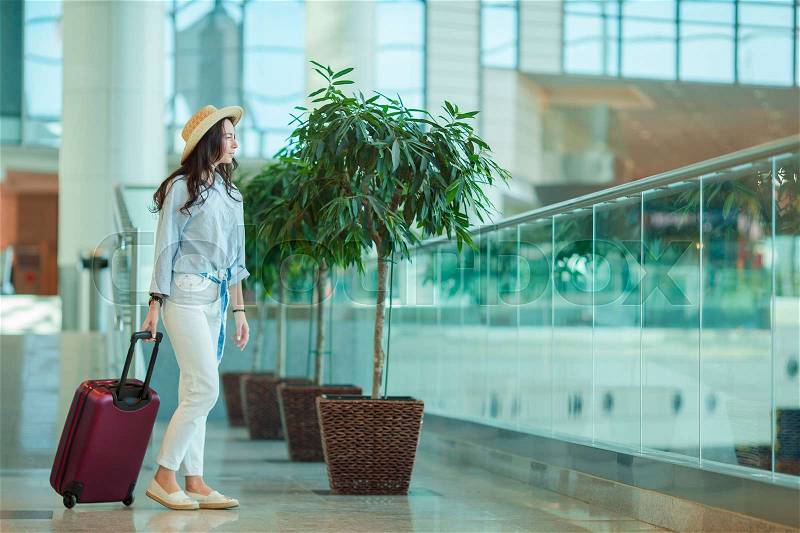 Young woman in hat with luggage in international airport. Airline passenger in an airport lounge waiting for flight aircraft, stock photo