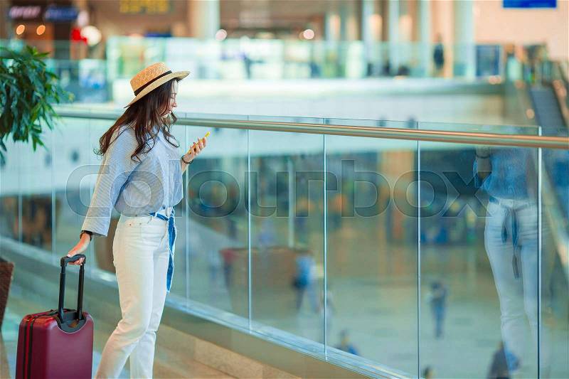 Young woman in hat with baggage in international airport walking with her luggage. Airline passenger in an airport lounge waiting for flight aircraft, stock photo