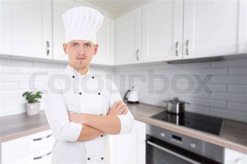 Young handsome chef man in uniform posing in modern kitchen, stock photo