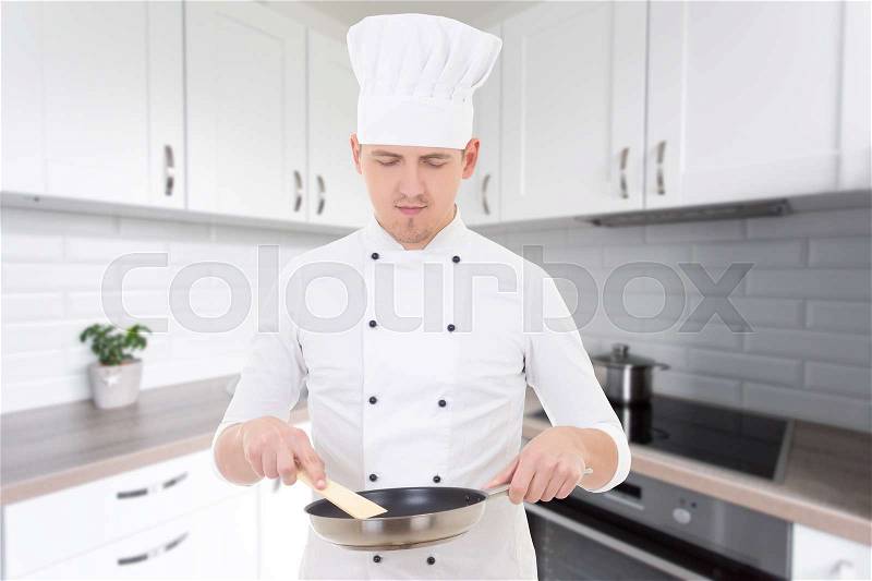 Portrait of man chef in uniform holding frying pan in modern kitchen, stock photo