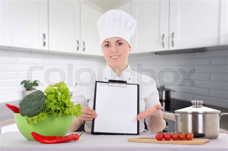 Portrait of attractive cook woman in uniform with clipboard sitting in the kitchen, stock photo