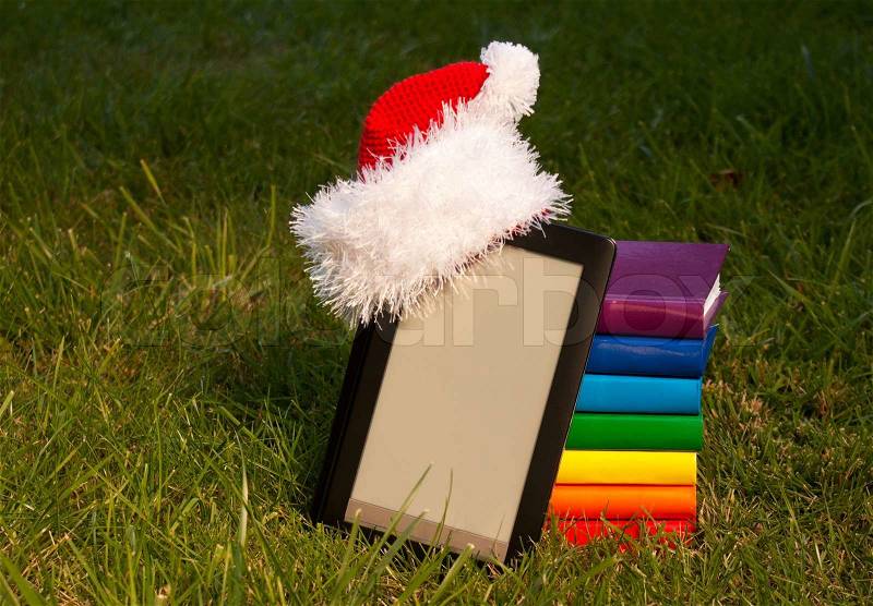 Electronic book reader wearing Santa\'s hat with stack of books, stock photo