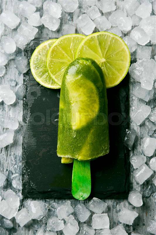 High-angle shot of a homemade mojito ice pop made with natural lime juice, rum, mint and lime slices, on a natural slate tray surrounded by ice, stock photo