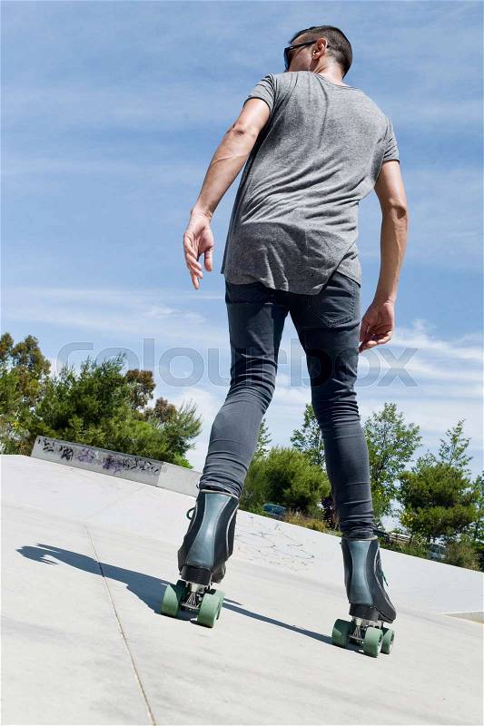 A young caucasian man roller skating backwards with quad skates in an outdoors skate park, stock photo