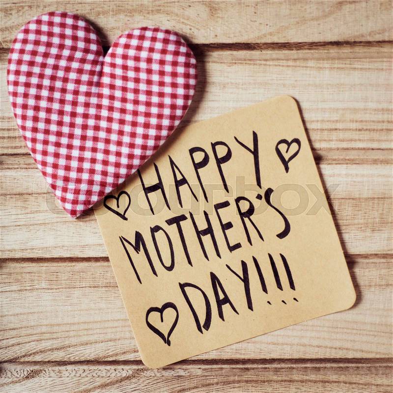 Closeup of a piece of paper with the text happy mothers day written in it and a fabric heart on a rustic wooden background, stock photo