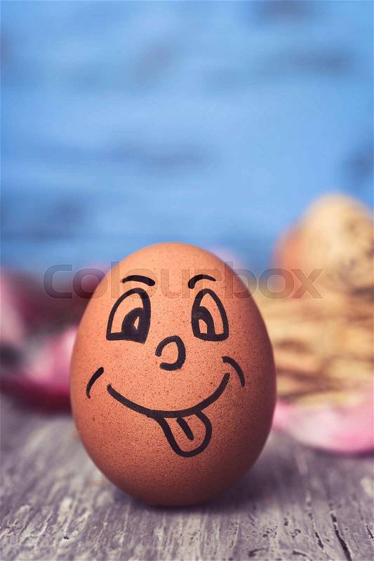 Closeup of a brown egg with a funny face on a rustic wooden surface, against a blue rustic wooden background, stock photo