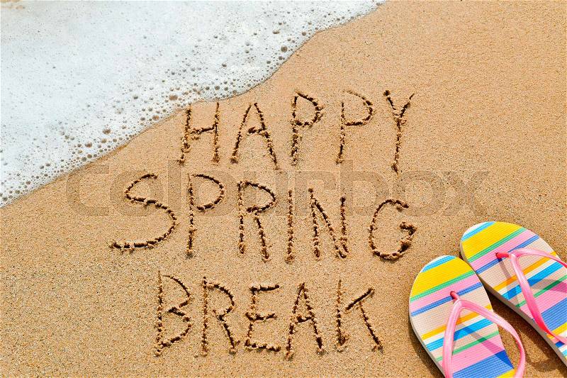 Closeup of the text happy spring break written in the sand of a beach and a pair of colorful flip-flops, stock photo